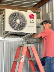 An HVAC technician installing an LG mini-split outdoor condenser unit on a wall for Carlsbad Heating & Cooling in Carlsbad, NM.