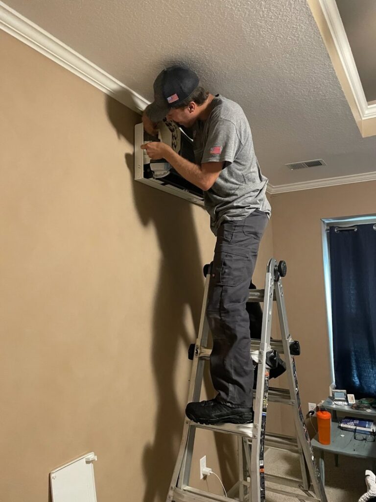 An HVAC technician on a ladder installing an indoor mini-split unit for Cool y Caliente HVAC Services in Bonner Springs, KS.