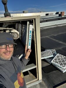 An HVAC technician installing new air filters in a commercial rooftop unit during maintenance for Four Corners Service Co. in Farmington, NM.