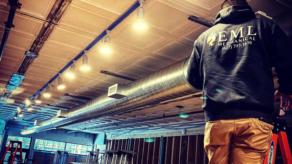 An EML Mechanical technician on a ladder installing spiral ductwork in a commercial space in Boston, MA.