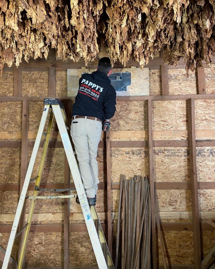 An HVAC technician from Pappy's Heating & Air INC installing a thermostat or control panel in Clayton, NC.
