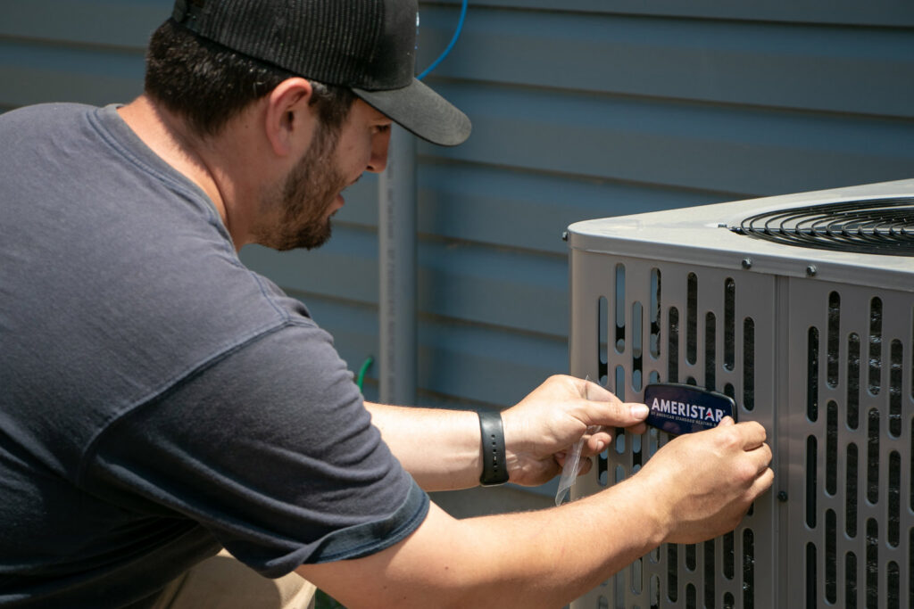 An HVAC technician applying a brand label to a new AC unit for Blue Fox Heating & Cooling in Lebanon, IN.