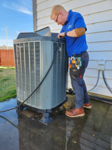 An HVAC technician performing maintenance on an outdoor air conditioning unit at Bowers Heating and Air Conditioning in Wichita, KS