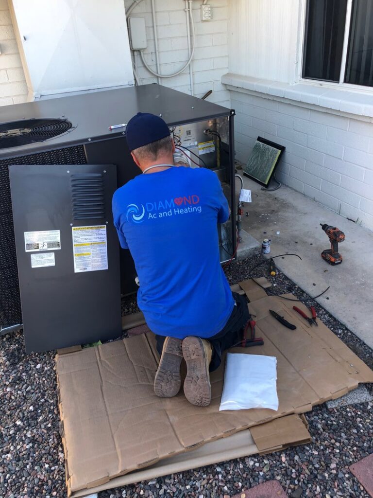 An HVAC technician performing maintenance on an outdoor AC unit for Diamond AC and Heating in Phoenix, AZ.