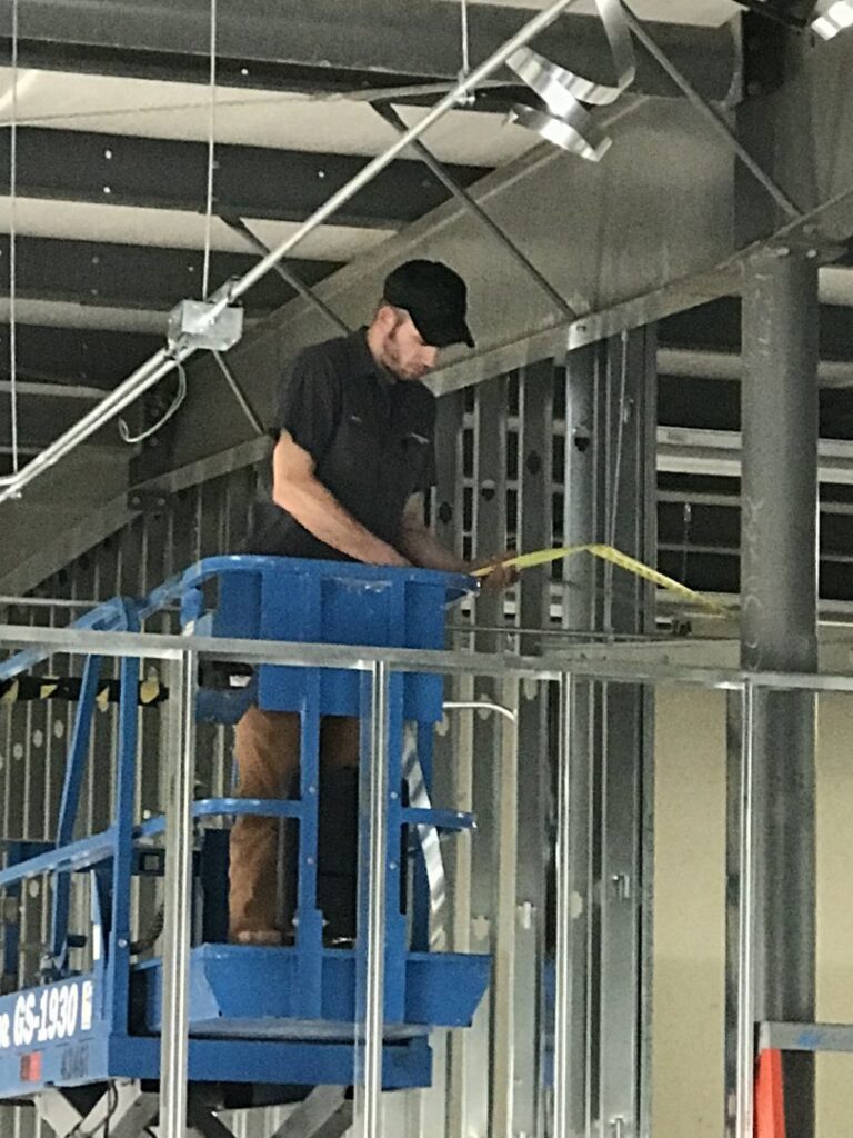 An HVAC technician on a scissor lift measuring for ductwork installation by A-1 Heating and Air Conditioning Service in Alexandria, VA