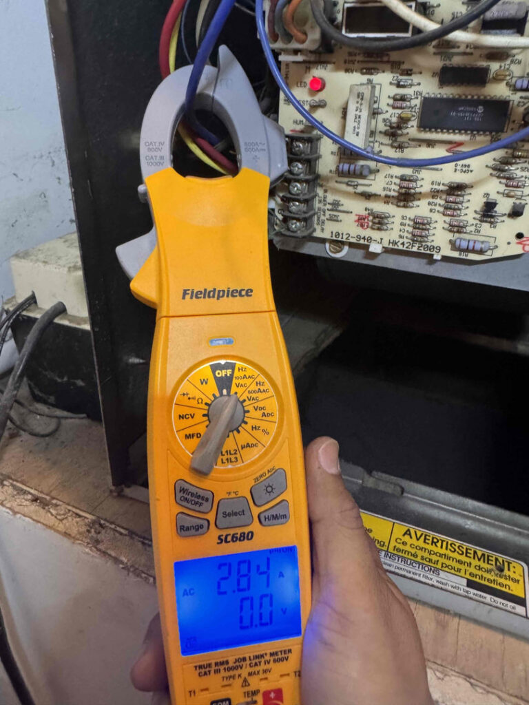 An HVAC technician measuring electrical current on a control board with a clamp meter for Affordable Heating and Air in Chatsworth, CA.