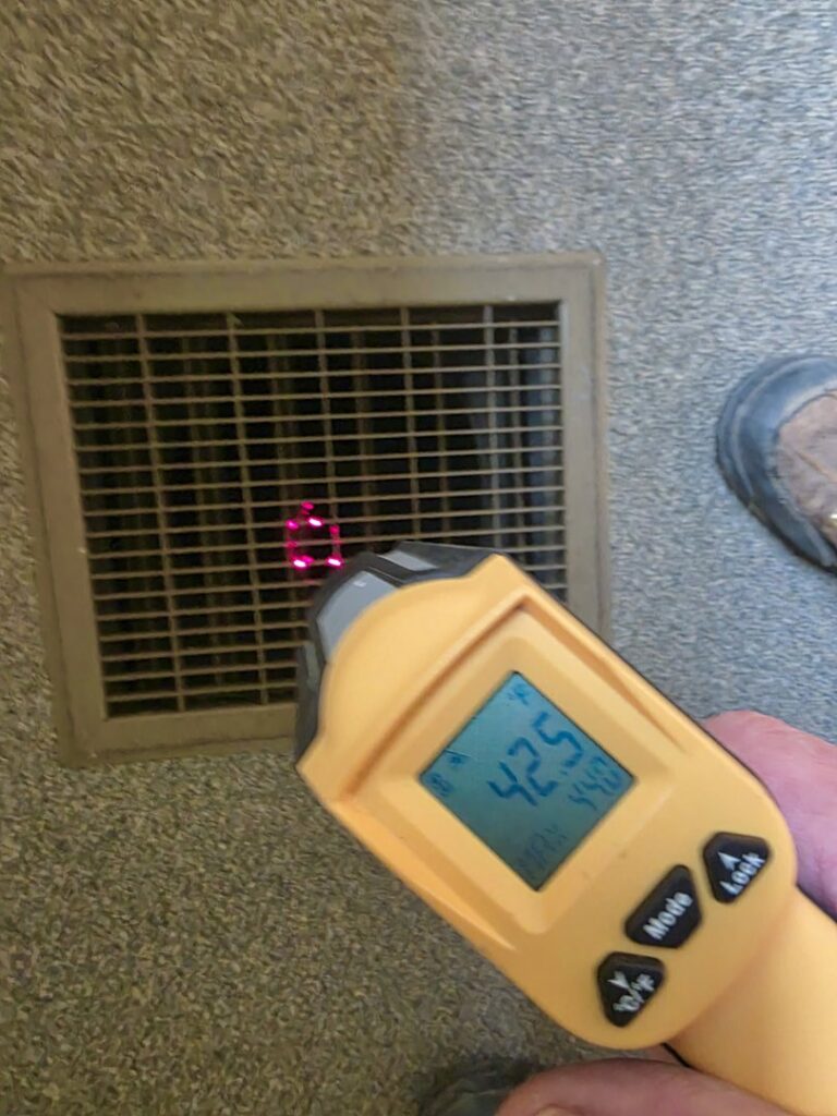 An HVAC technician measuring air vent temperature with an infrared thermometer for diagnostic purposes by Bruce Heating & Air in Kennewick, WA.