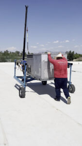 An HVAC technician from Arrow Pro Services moving a rooftop unit on a cart across a commercial roof in Gilbert, AZ