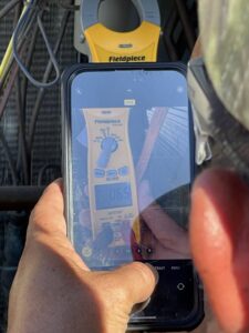 An HVAC technician capturing a multimeter reading on a phone during service by South Texas Climate Control in San Antonio, TX