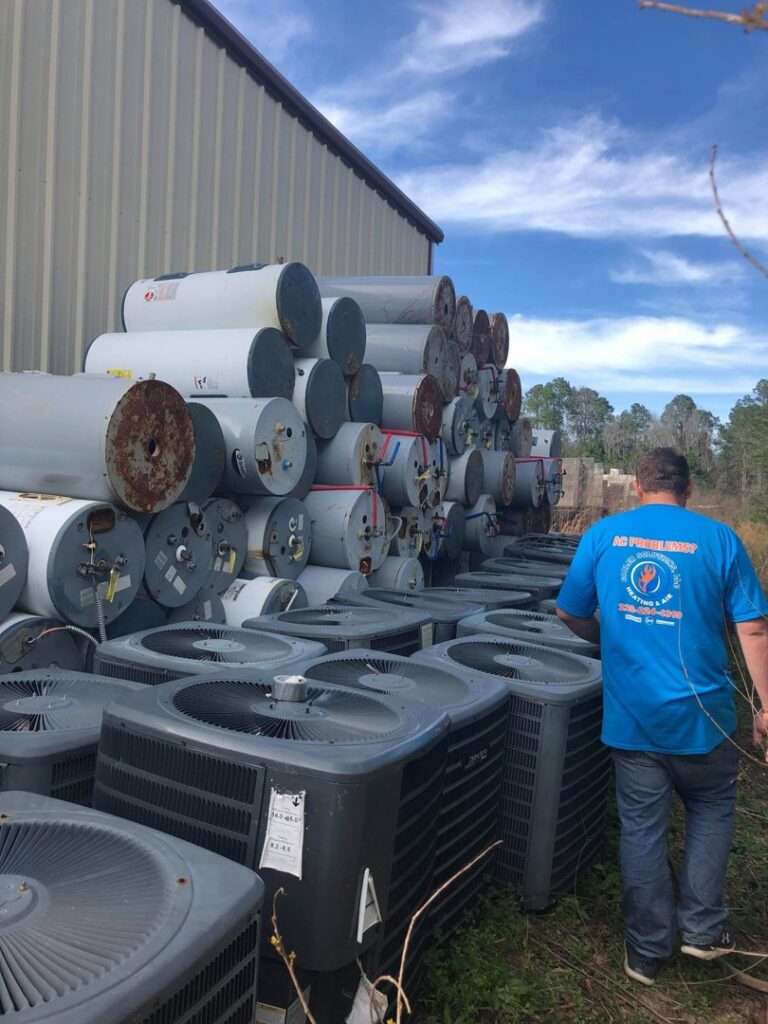 An HVAC technician walking past a large stack of old water heaters and AC units for disposal by Cooler Solutions LLC Heating & Air in Gulfport, MS.
