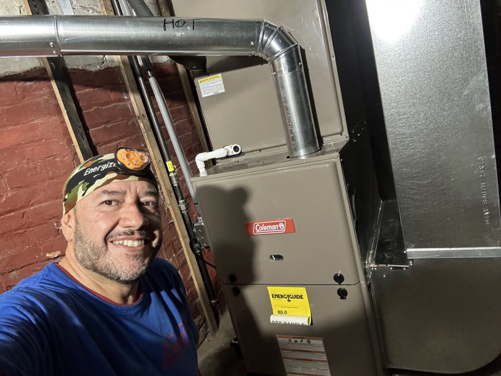 An HVAC technician smiling next to a newly installed furnace by Nacho Heating & Cooling Plus Co. in Crest Hill, IL