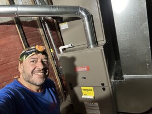 An HVAC technician smiling next to a newly installed furnace by Nacho Heating & Cooling Plus Co. in Crest Hill, IL