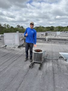 An HVAC technician standing next to an old air conditioning unit on a commercial rooftop in Jacksonville, FL, by Whitleys Heating and Air.