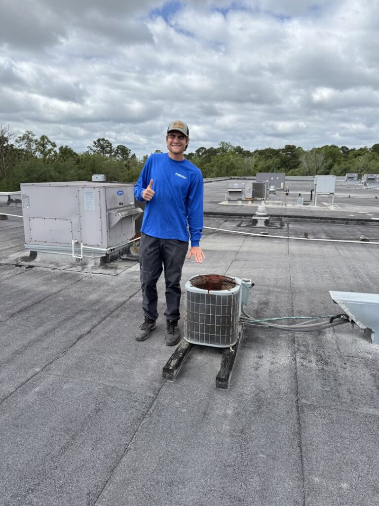 An HVAC technician standing next to an old air conditioning unit on a commercial rooftop in Jacksonville, FL, by Whitleys Heating and Air.