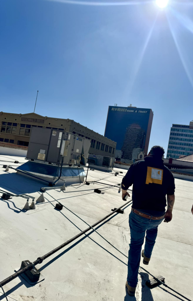An HVAC technician walks on a commercial rooftop near HVAC units for NM Heating and Air in Albuquerque, NM.