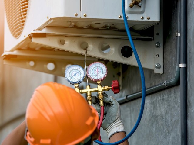An HVAC technician on a ladder repairing an indoor AC unit for ChillTek AC Repair Glendale in Glendale, AZ.