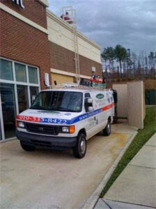 An HVAC technician on a ladder accessing a roof for service, with a branded van from Environmental Heating & Air NC in Cary, NC.