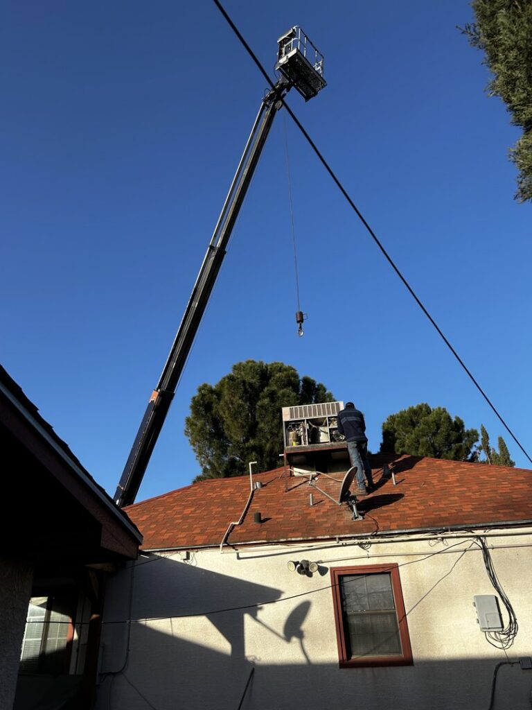 An HVAC technician working on a rooftop unit with a crane in the background, performing service for Carlsbad Heating & Cooling in Carlsbad, NM.