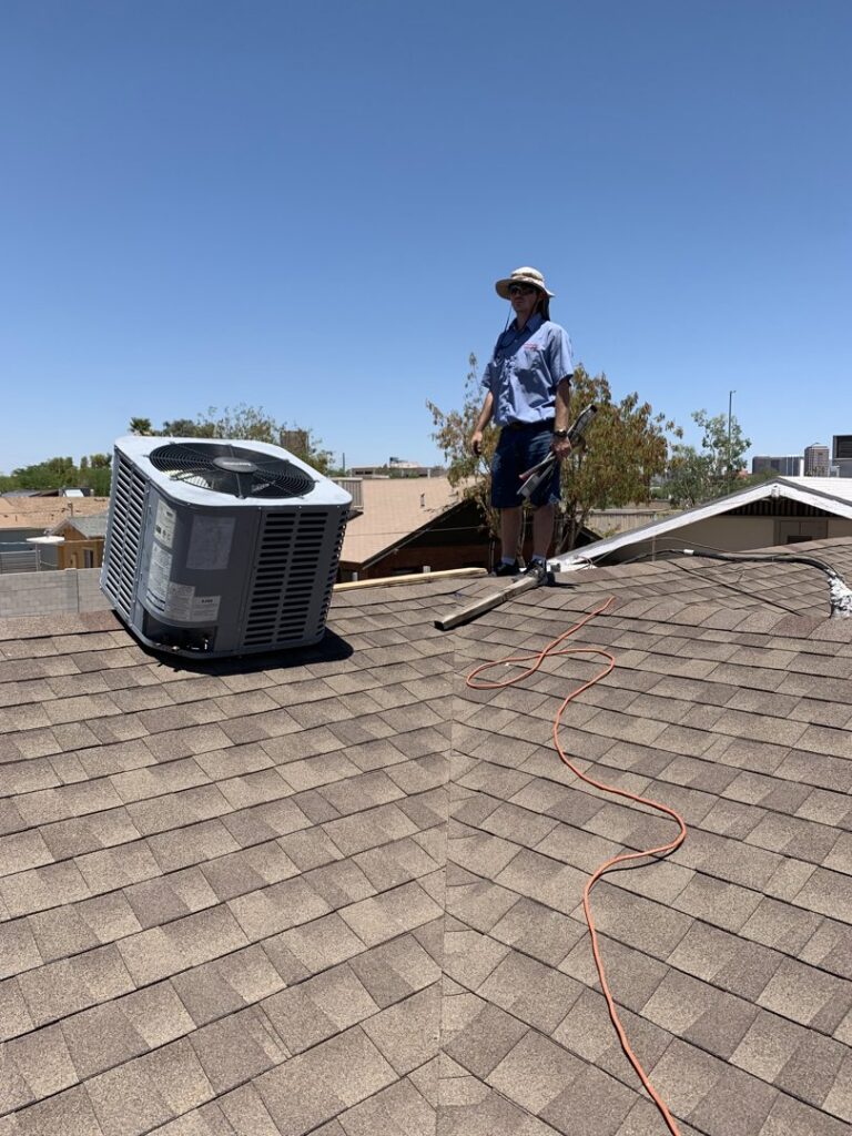 An HVAC technician on a roof inspecting an outdoor unit for Advanced Comfort A/C & Heating in Phoenix, AZ.