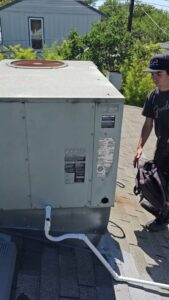 An HVAC technician on a roof next to a large commercial unit, ready to perform service for Ecology Air Innovations in Sacramento, CA.