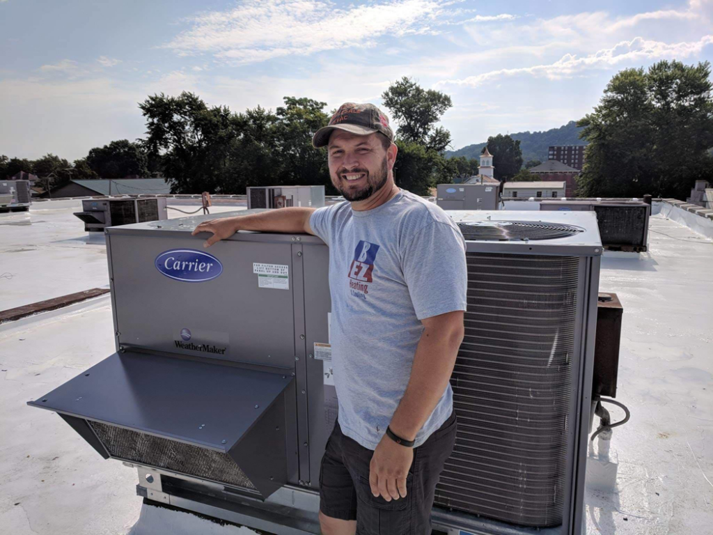 An HVAC technician from B E Z Heating and Cooling on a rooftop with a Carrier commercial HVAC unit in Huntington, WV.
