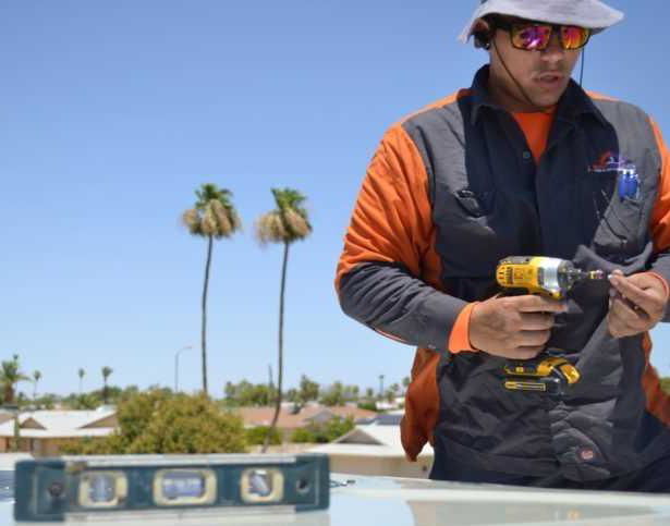 An HVAC technician on a rooftop holding a drill, performing service for 1 800 Cooling, INC in Phoenix, AZ.