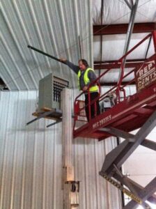 An HVAC technician on a scissor lift working on a large overhead heating unit inside a commercial building for KATS Heating & Cooling in La Grange Park, IL.