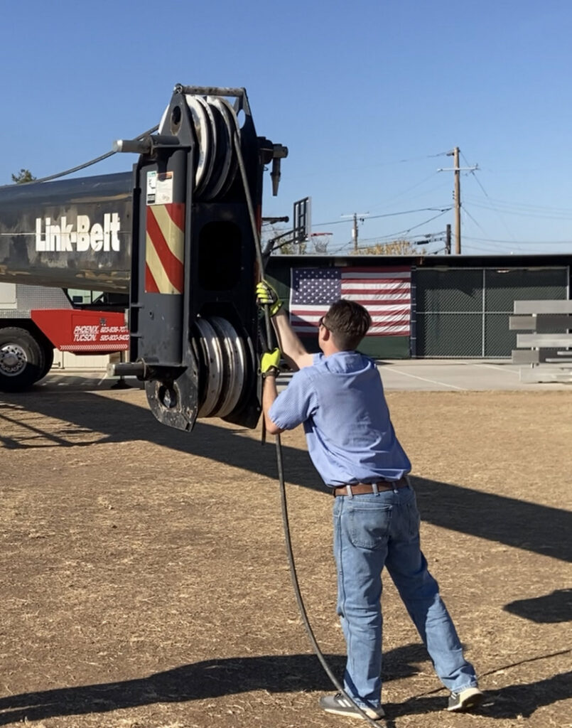 An HVAC technician operating a crane, likely for unit installation, for Advanced Comfort A/C & Heating in Phoenix, AZ.