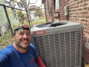 An HVAC technician smiling next to an outdoor air conditioning unit by Nacho Heating & Cooling Plus Co. in Crest Hill, IL