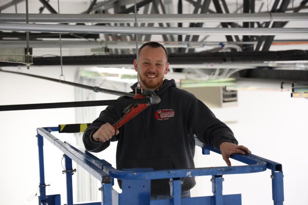 An HVAC technician working on overhead ductwork in a commercial building for The Heating Specialist in Portland, OR