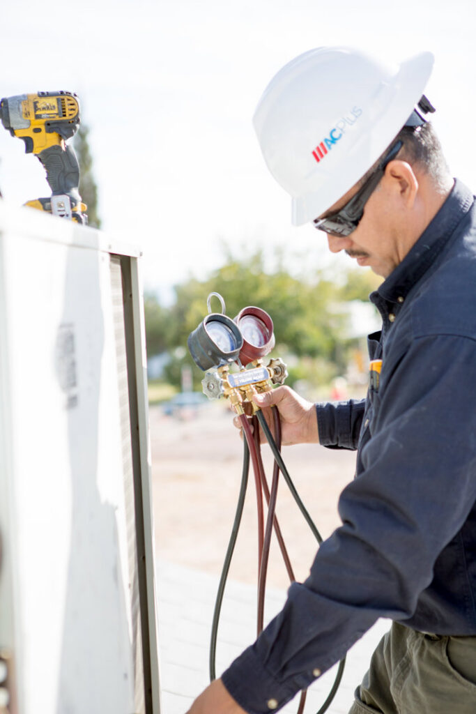 An HVAC technician performing maintenance on an outdoor AC unit for AC Plus Heating & Air Conditioning Service in Las Vegas, NV.