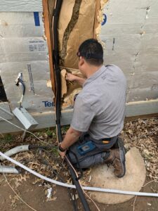 An HVAC technician working on refrigerant lines and wiring during an installation or repair for OKIE Heating and Cooling in Tulsa, OK.