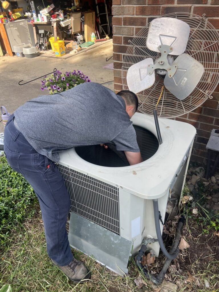 An HVAC technician performing repairs inside an outdoor AC condenser unit for Radiant Heating & Cooling in Fishers, IN.