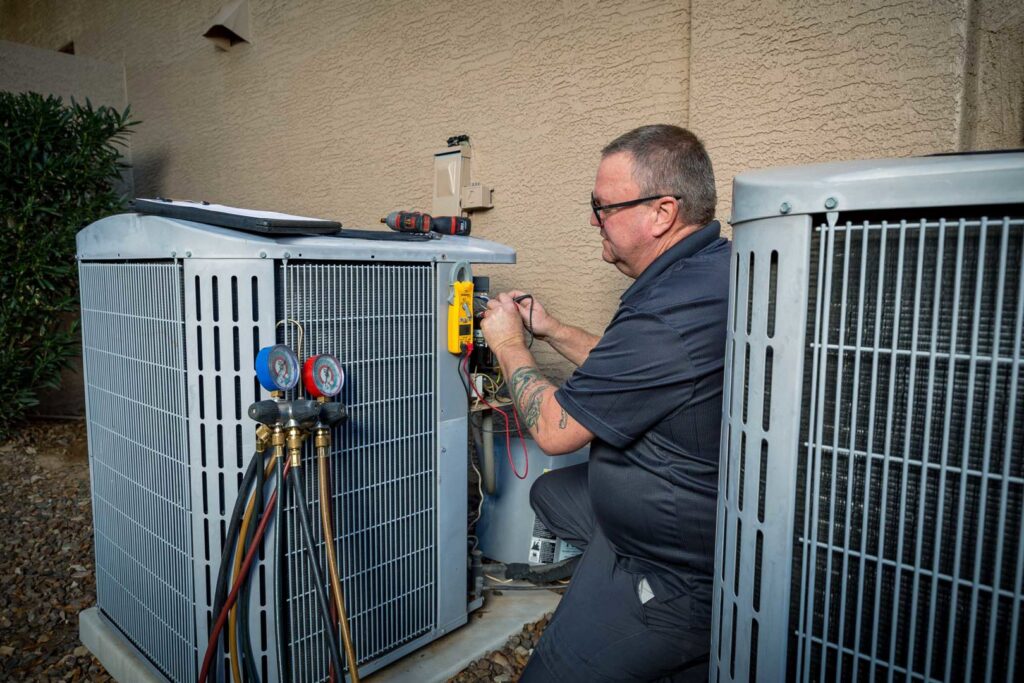 An HVAC technician repairing an outdoor AC unit with a multimeter at AVI Heating & Cooling in Surprise, AZ.