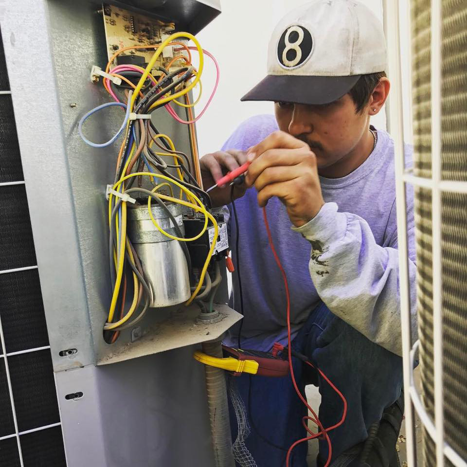 An HVAC technician repairing an outdoor air conditioning unit with a multimeter for Barry's A/C in Lafayette, LA.
