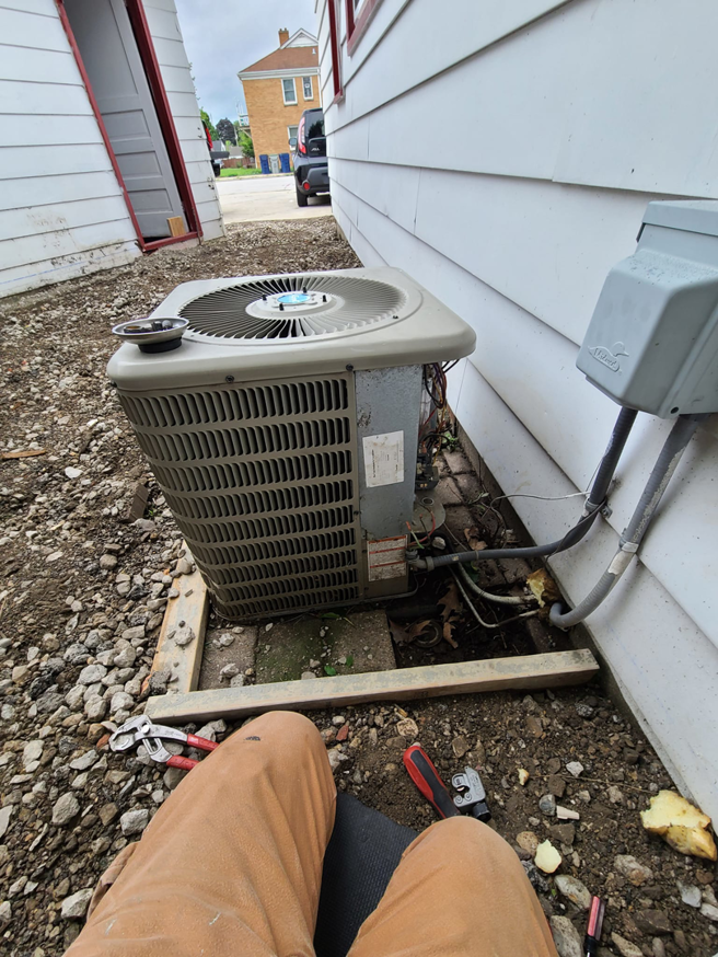 An HVAC technician repairing an outdoor air conditioning unit with tools on the ground by Guzman Heating & Cooling in Milwaukee, WI.