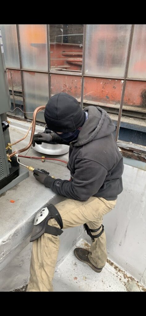 An HVAC technician performing service or repair on an outdoor air conditioning unit for JL Heating & AC LLC in Chicago, IL