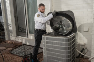 An HVAC technician from One Hour Heating & Air Conditioning of Lancaster, PA, repairing an outdoor air conditioning unit with the top cover removed.