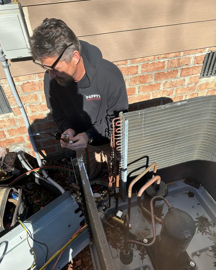 An HVAC technician from Pappy's Heating & Air INC repairing an outdoor AC condenser unit in Clayton, NC.