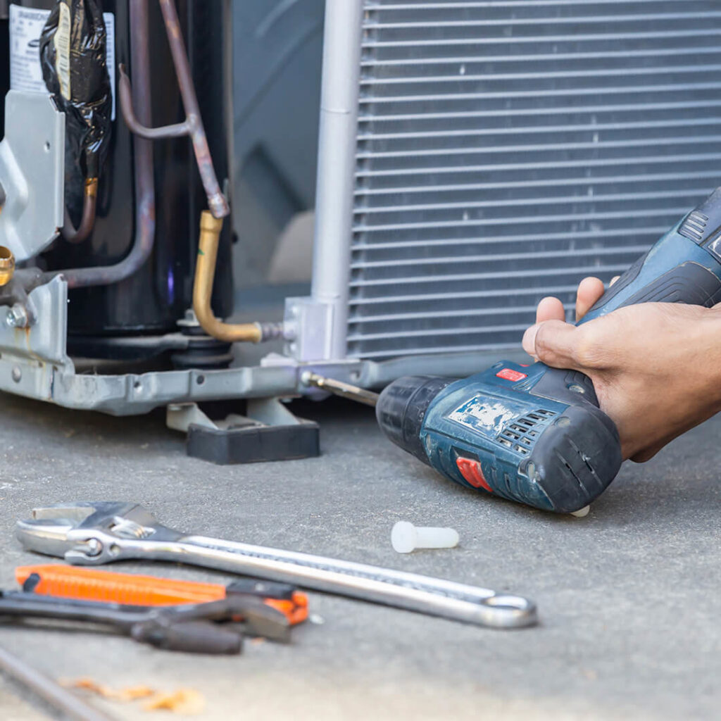 An HVAC technician using a power drill to repair an outdoor AC unit for Premier Comfort Service Company in San Antonio, TX.