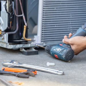 An HVAC technician using a power drill to repair an outdoor AC unit for Premier Comfort Service Company in San Antonio, TX.
