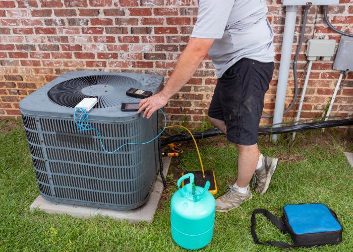 An HVAC technician repairing an outdoor AC unit with a refrigerant tank for Rhode Island HVAC Services in Providence, RI.