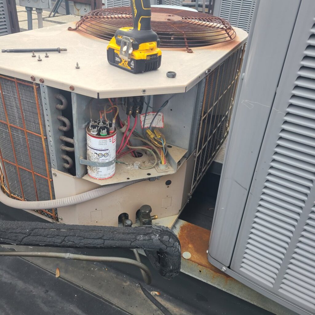 An HVAC technician repairing an outdoor air conditioning unit, showing internal components, by Your HVAC Guy in Aurora, IL.