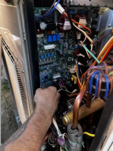 An MB Heating and Air technician repairing the internal circuit board of an HVAC unit in Northridge, CA.