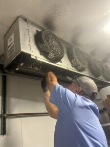 An HVAC technician performing repairs on a commercial refrigeration unit inside a walk-in cooler at Four Corners Service Co. in Farmington, NM.