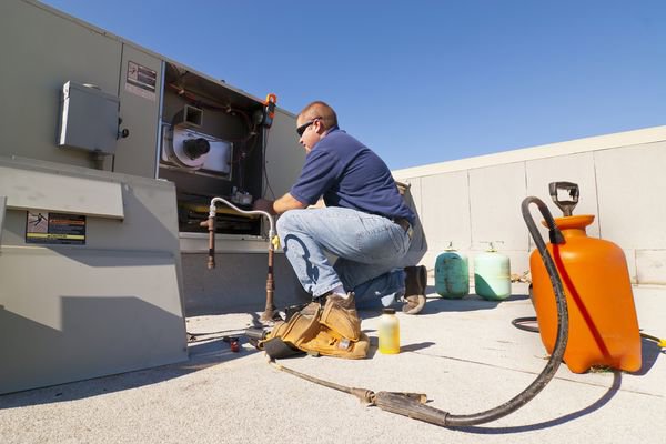 An HVAC technician repairing a commercial rooftop unit with tools nearby for General Air Conditioning Service Corp in Greenville, SC.
