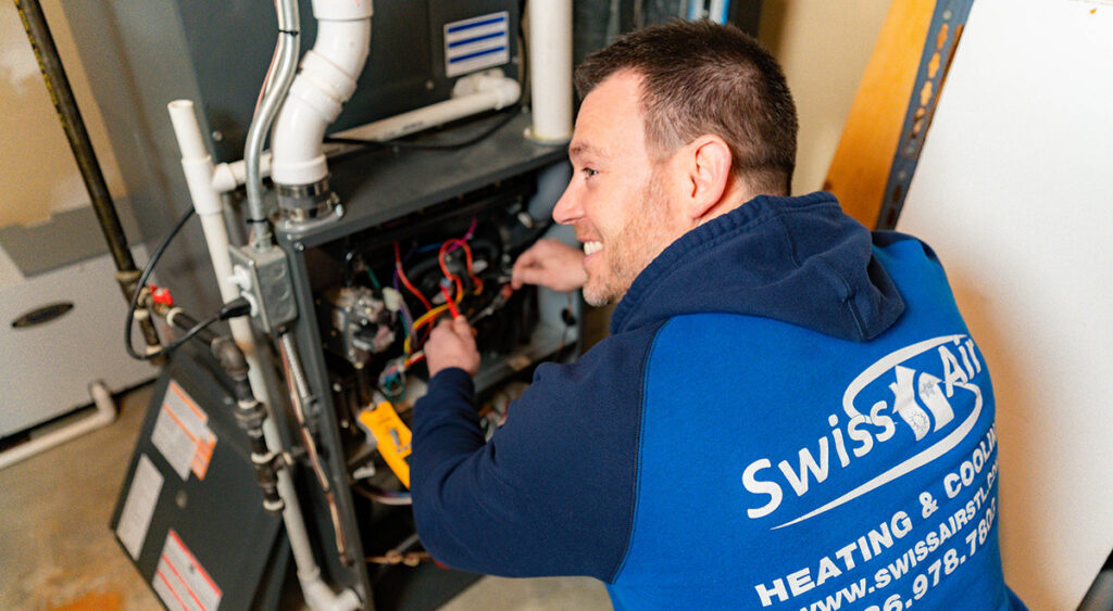 A skilled HVAC technician from Swiss Air Heating & Cooling performing repairs on a furnace in O'Fallon, MO.