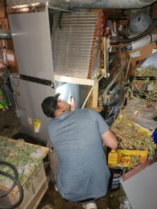 An HVAC technician repairing an indoor furnace or air handler unit in a residential basement for Dad's Heating and Cooling in Blue Springs, MO.