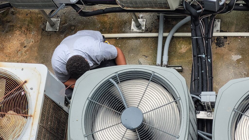 An HVAC technician performing maintenance or repair on an outdoor air conditioning unit, provided by Jons-Air in Carmel, IN.
