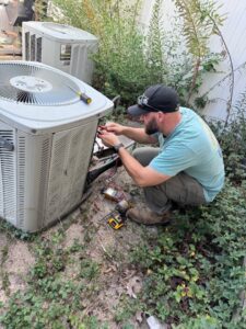 An ARKLA AIR LLC technician repairing an outdoor air conditioning unit with a multimeter in Springhill, LA.